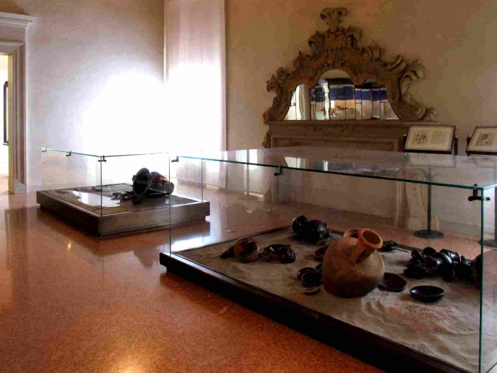 La sala XIV del Museo, simbolo del pregio sia del contenuto che del contenitore: in primo piano, la ricostruzione di due sepolture spinetiche e, sullo sfondo, il camino con specchi e stucchi barocchi